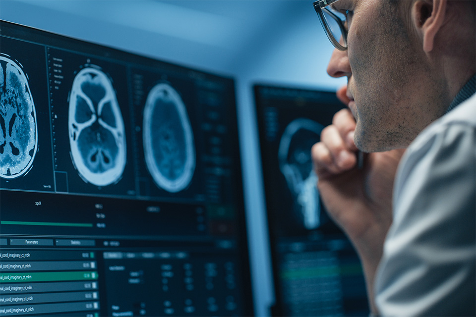 Ein Radiologe sitzt an einem professionellen Arbeitsplatz mit mehreren Monitoren und analysiert digitale Röntgenaufnahmen oder MRT-Bilder im Rahmen der Teleradiologie.