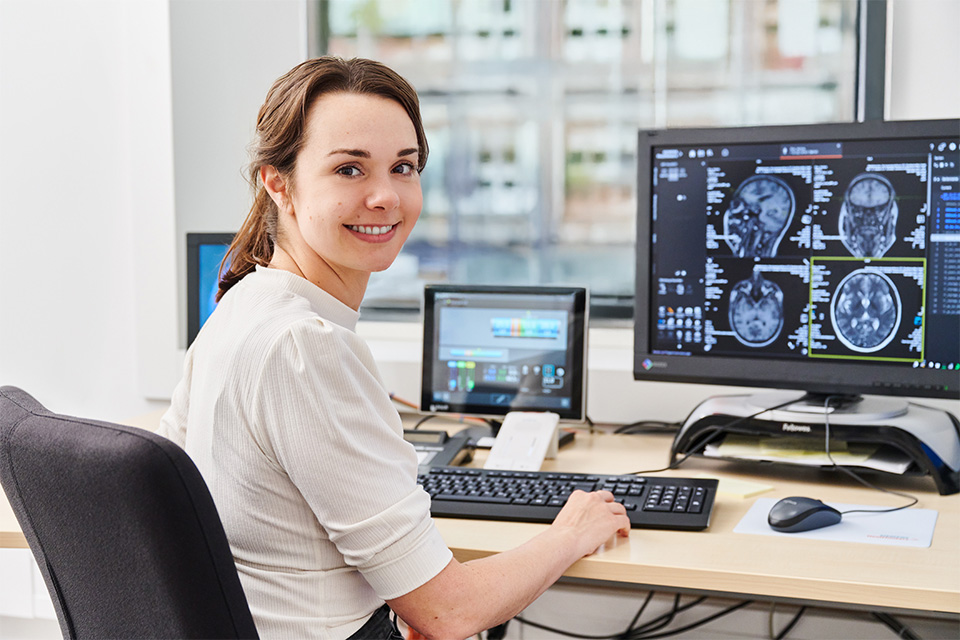 Porträt einer lächelnden Mitarbeiterin an einem modernen radiologischen Diagnose-Arbeitsplatz mit spezialisierten Monitoren für die Bildauswertung.