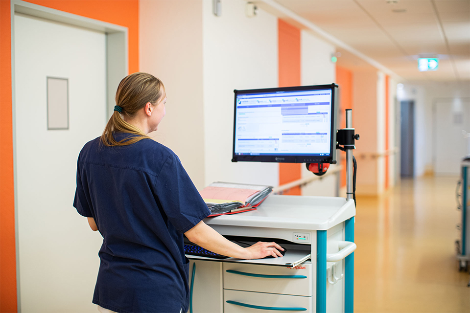 Trägerkranken-haus Pflegekraft in blauer Arbeitskleidung steht an einem Computerwagen in einem Krankenhausflur