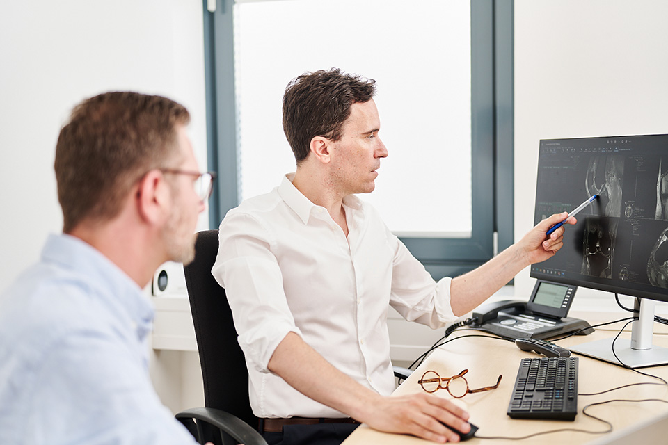 Prof. Florian Streitparth bespricht mit einem Kollegen die medizinische Bildgebung auf einem Monitor.